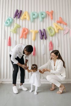 A joyful family celebrates their baby's birthday with colorful balloons and smiles.