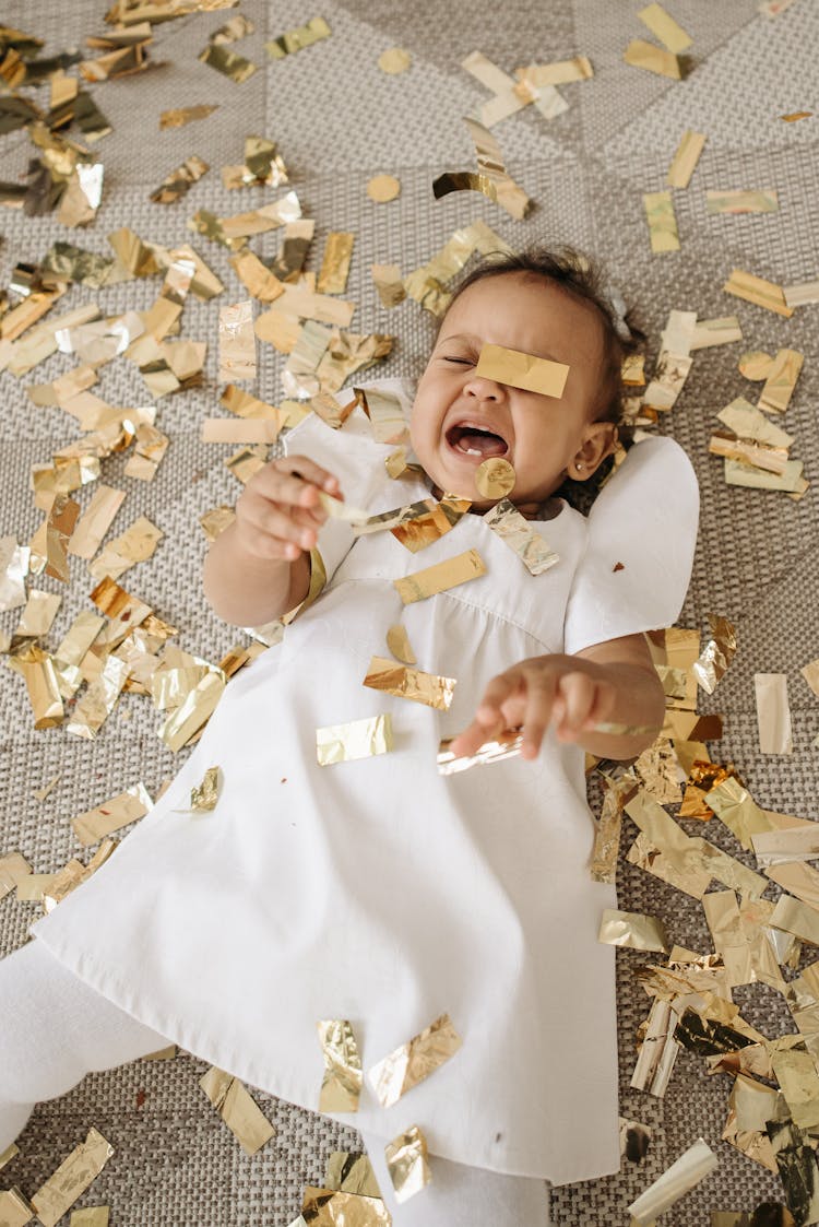 Crying Baby In White Dress Lying On The Ground Full Of Confetti 