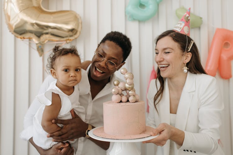 Man Holding A Baby While The Woman Is Holding A Cake 