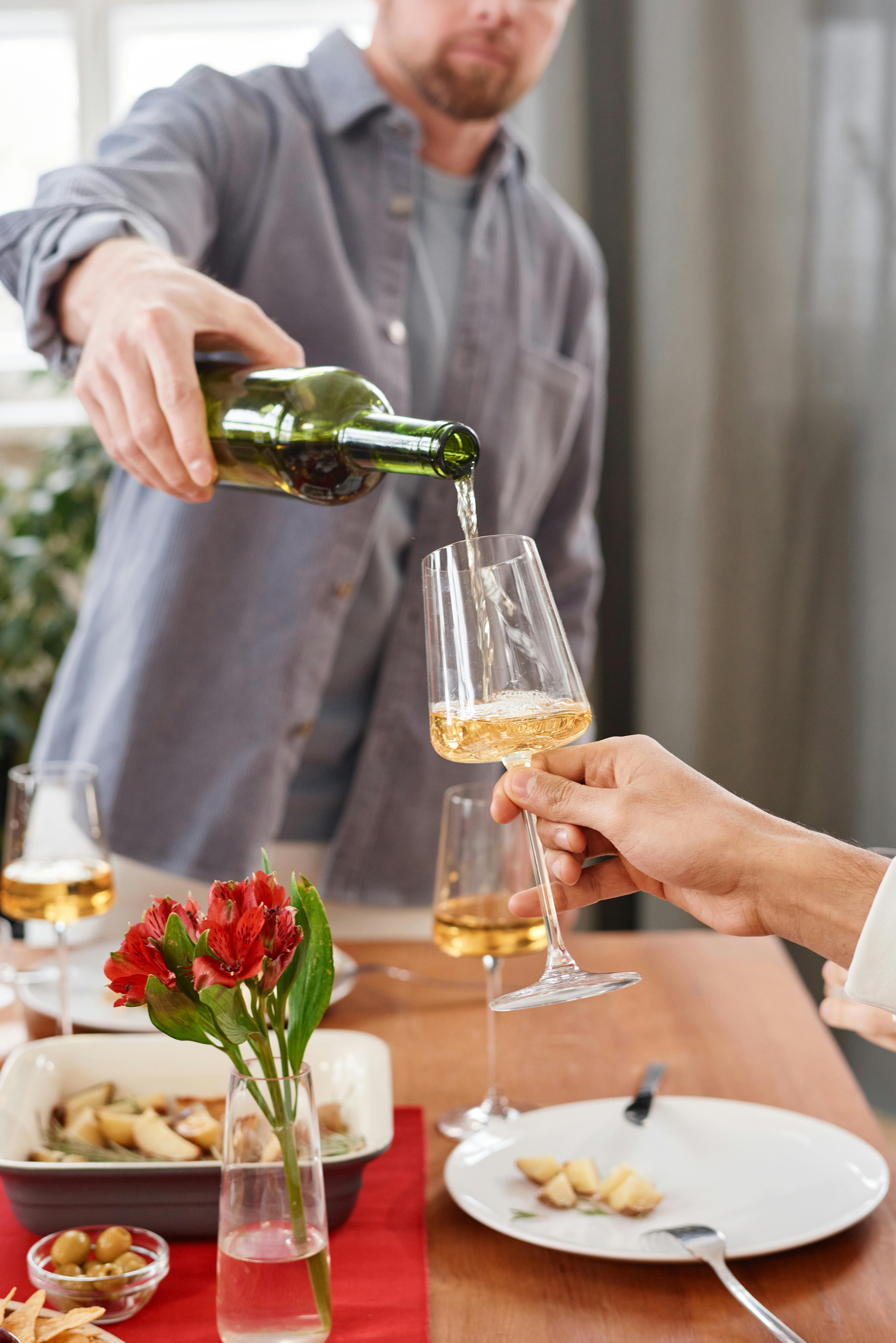Glass of white wine being poured during a casual indoor meal setting.