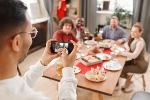 A person photographing a cheerful family gathering with a smartphone indoors.