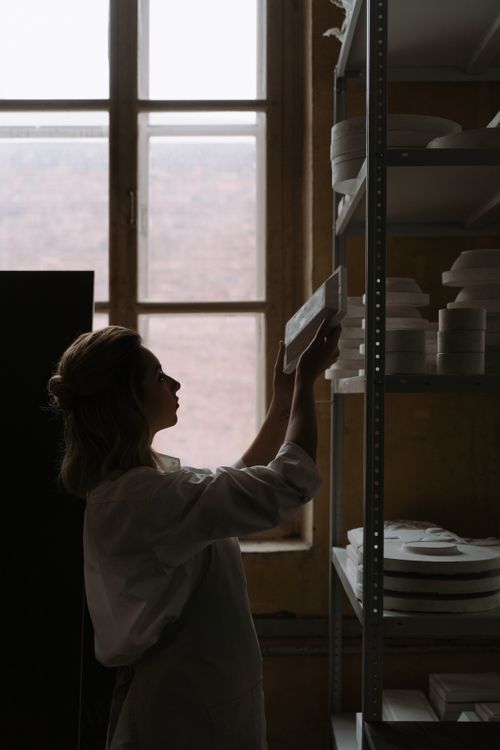 Free An artisan organizing ceramic plates on shelves against a distant window. Stock Photo