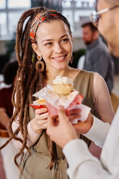 Free Young woman with dreadlocks holding a cupcake and smiling indoors, expressing joy and camaraderie. Stock Photo