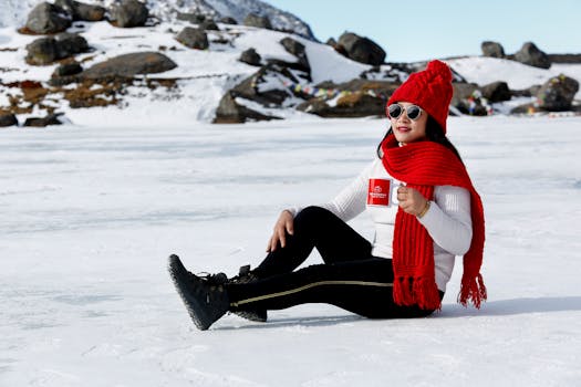 A woman in a red scarf and beanie enjoys a snowy landscape, holding a ceramic mug.