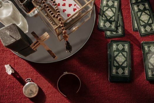A close-up of tarot cards, rosary, and symbolic items on a red surface, capturing a mystical vibe.