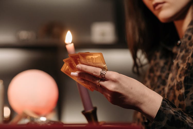 A Woman Beside A Lighted Candle Holding Gold Cards