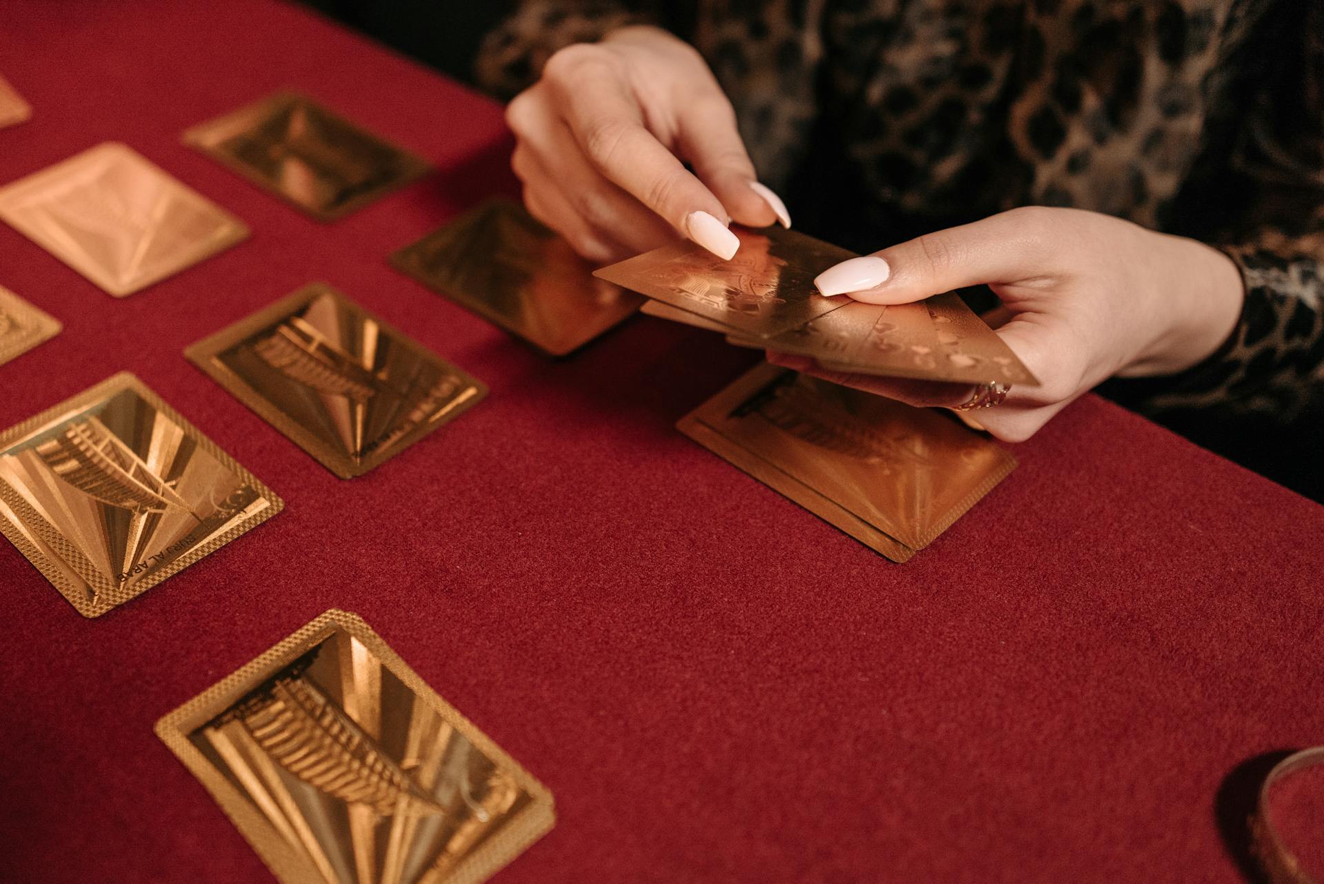 A close-up of hands holding gold cards while playing a card game on a red table. Perfect for gaming and leisure themes.