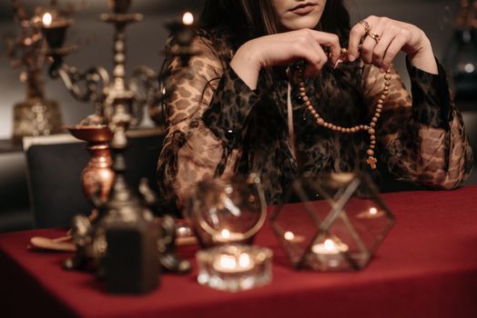 A woman in a mystical setting holding a rosary, surrounded by occult objects.
