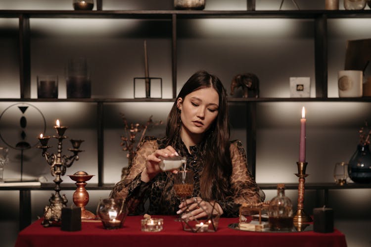 Woman Sitting By A Table Pouring Liquid Into A Glass