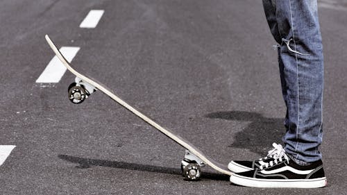 Close-up of a Man Standing on a Street and Lifting a Skateboard with His Leg 