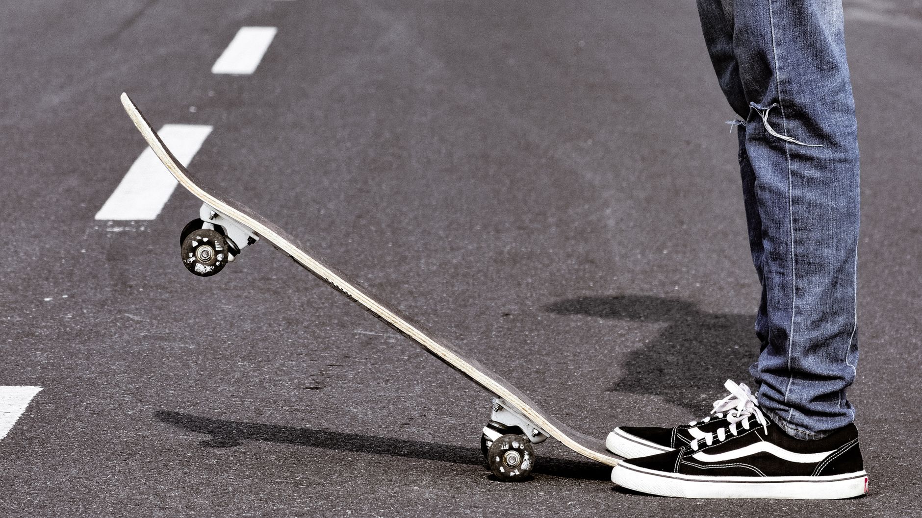 Close-up of a skateboarder balancing on an asphalt road wearing denim jeans and Vans shoes.