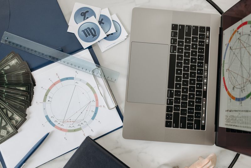 Astrology chart, laptop and cards on a desk for celestial analysis