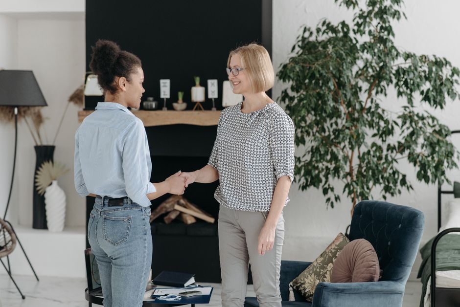 the importance of digital etiquette in hybrid workplaces - Two women in a stylish interior shake hands, symbolizing agreement in a modern office setting.
