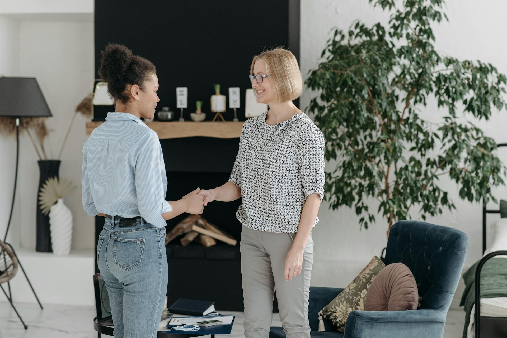 Two women in a stylish interior shake hands, symbolizing agreement in a modern office setting.