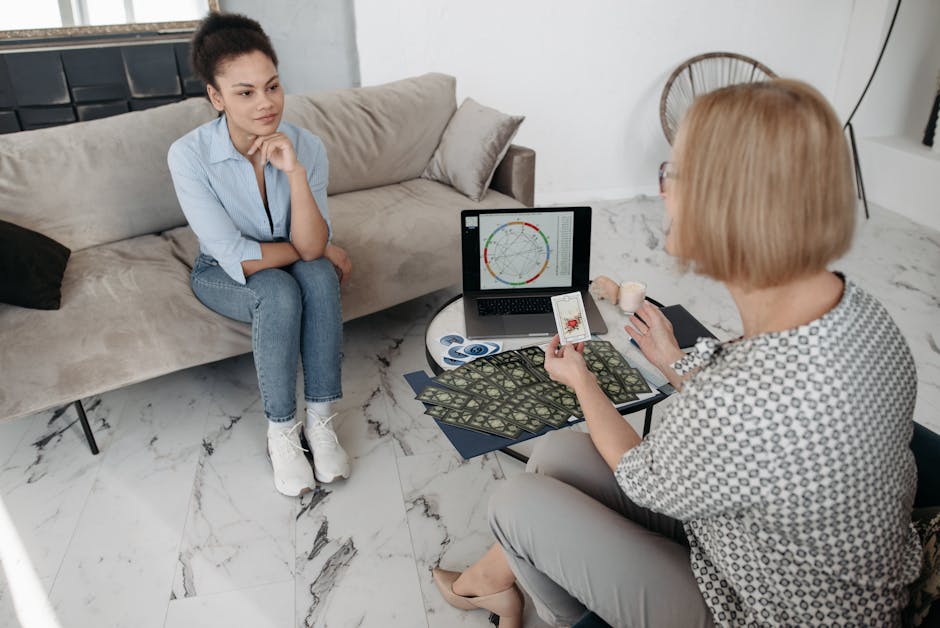 Women discuss astrology with a natal chart and tarot cards on a couch.