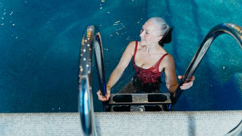 Elderly woman in a red swimsuit smiling while exiting a swimming pool.