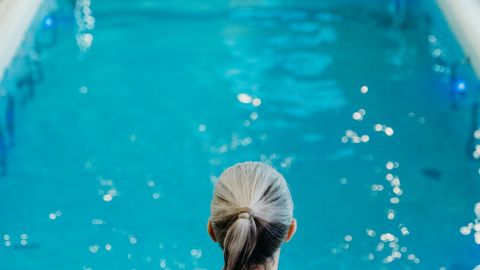 Back view of a woman in a red swimsuit by an indoor swimming pool, ready to dive.