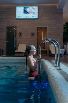 An elderly woman in a red swimsuit enjoying a swim in an indoor pool, embodying leisure and relaxation.