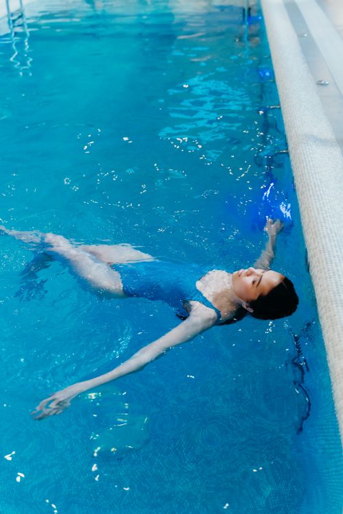 Free Woman in a swimsuit floating in a serene indoor swimming pool, enjoying leisure time. Stock Photo