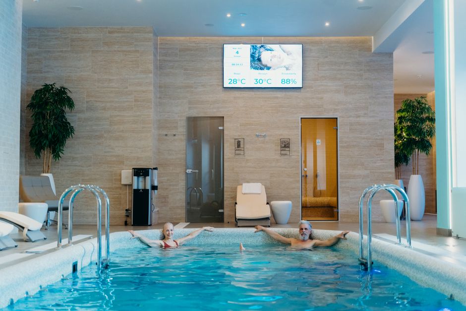 Stel in een wellnesszwembad met saunadeuren op de achtergrond