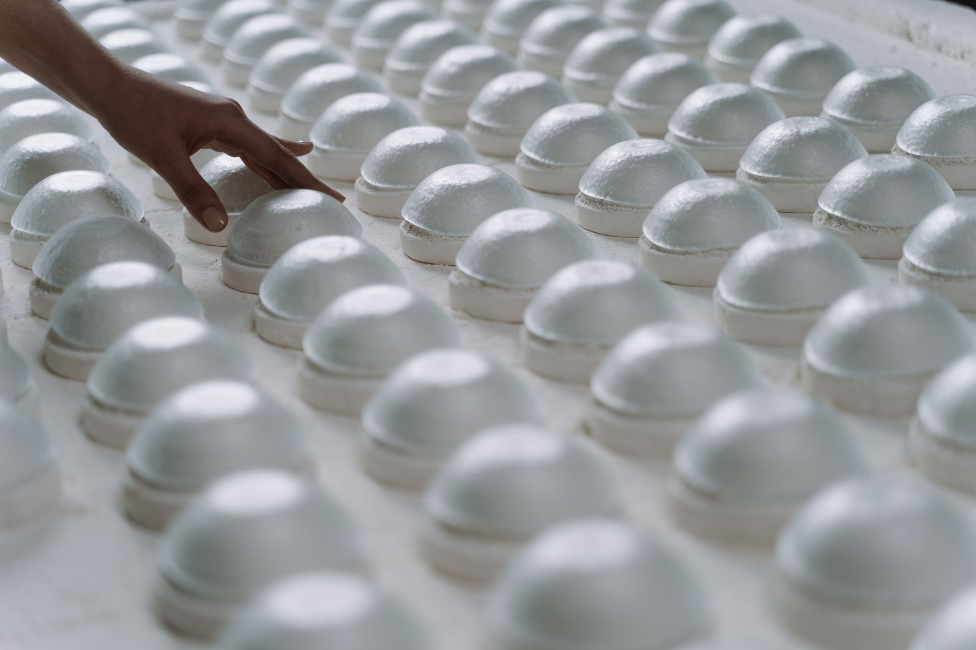 A person gently inspects rows of ceramic molds in a factory setting.