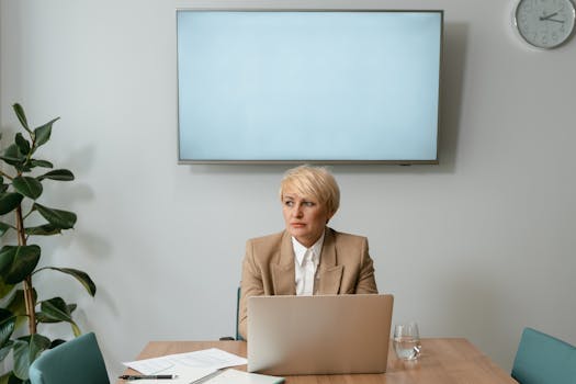 Woman in a business attire sitting at a desk with a laptop, pondering.