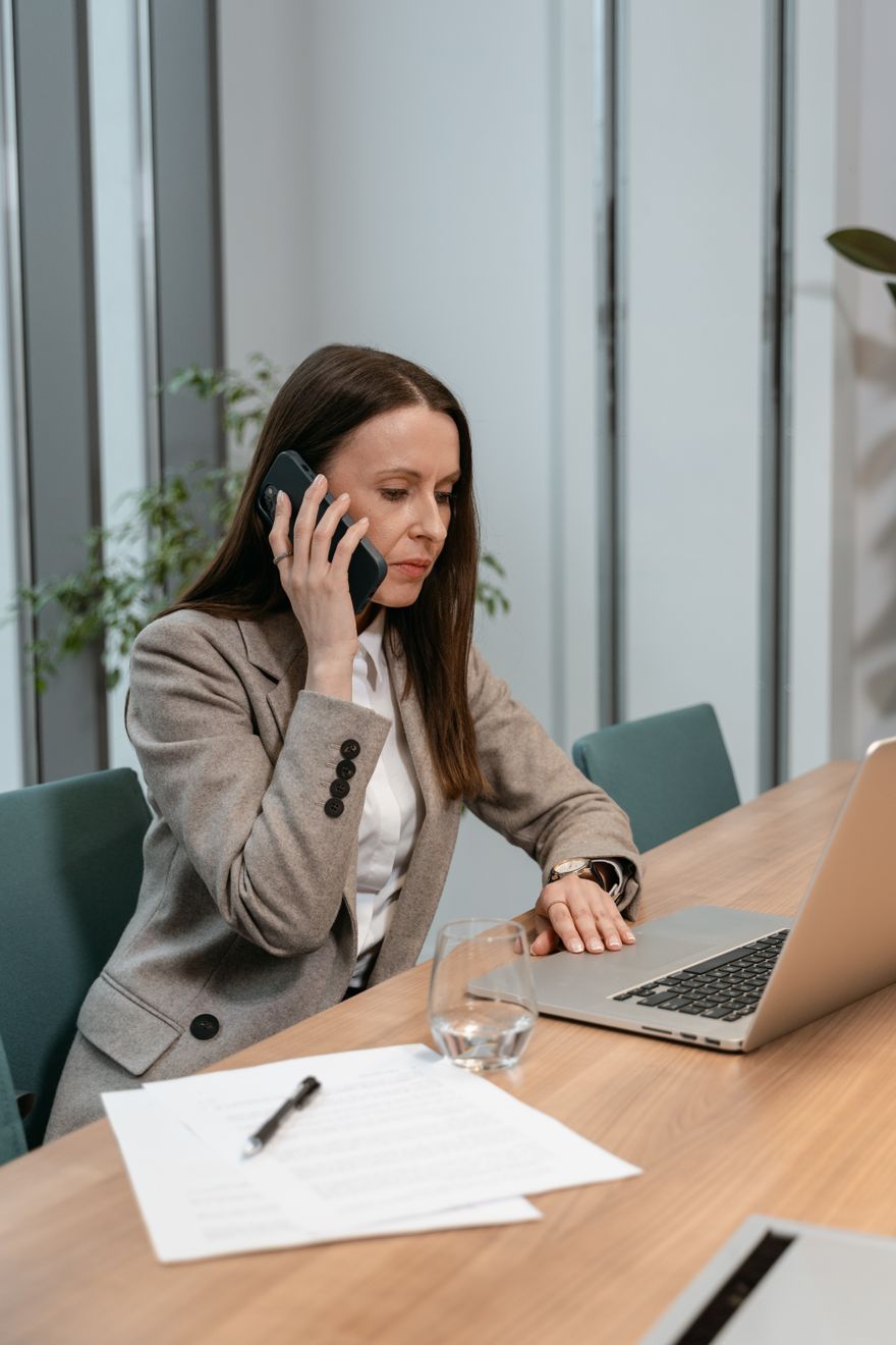 An analyst takes a call at a shared desk while reviewing a contract — photo by MART PRODUCTION on Pexels