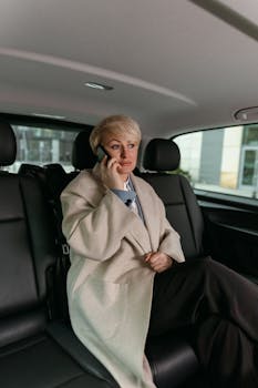 Confident woman in a beige coat making a phone call inside a luxury car.