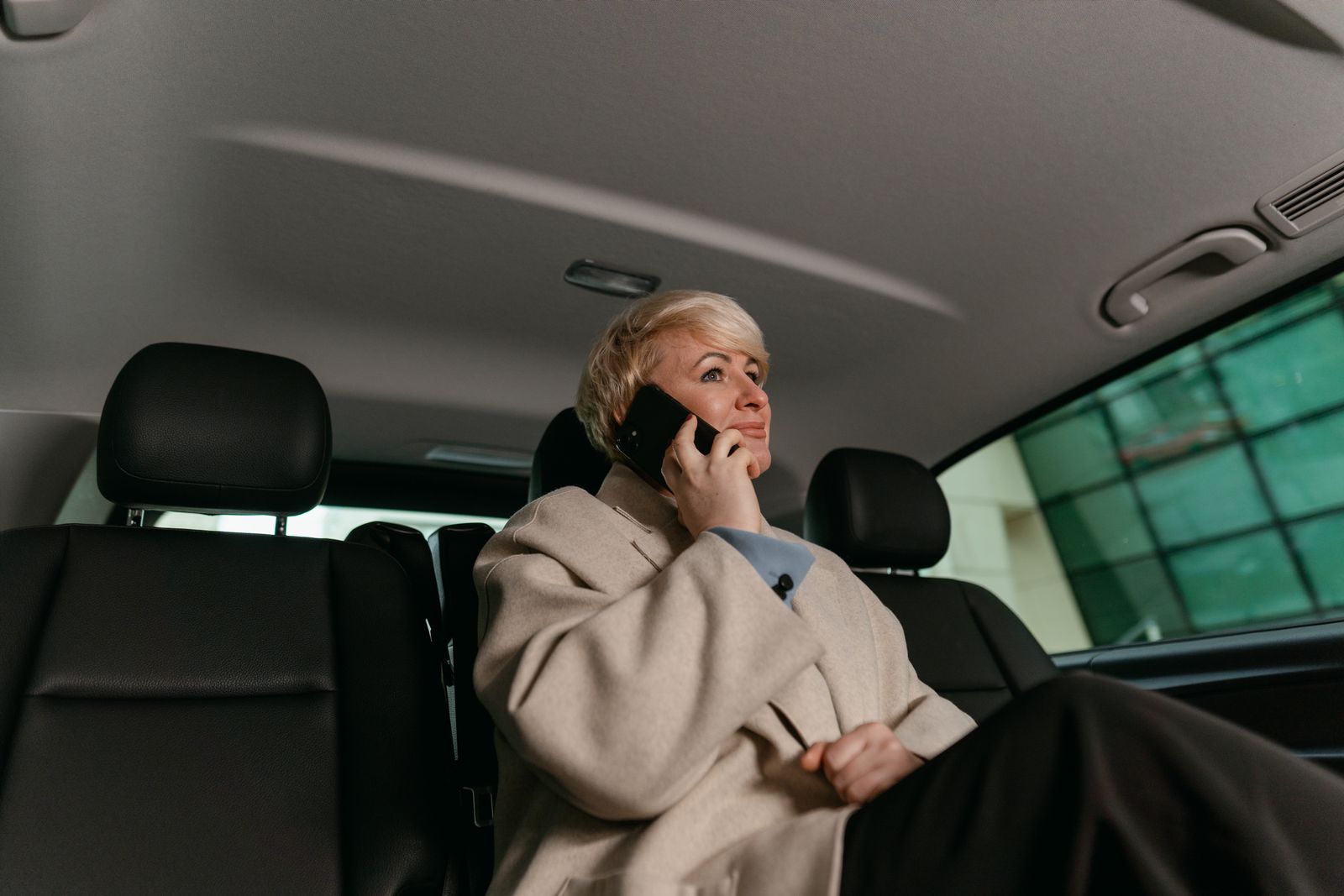 A woman in a brown coat making a phone call while sitting in a car