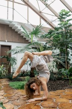 A woman performs a graceful yoga handstand indoors surrounded by lush plants.
