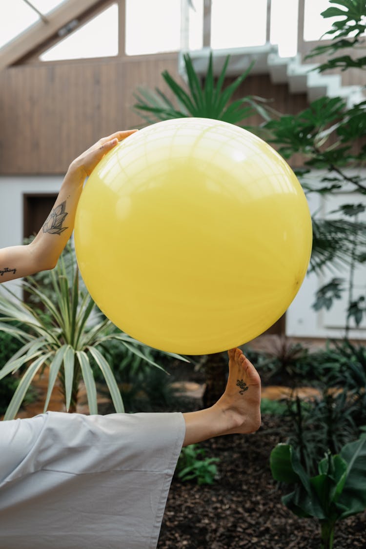 Unrecognizable Person Holding Big Yellow Ball With Hand And Foot