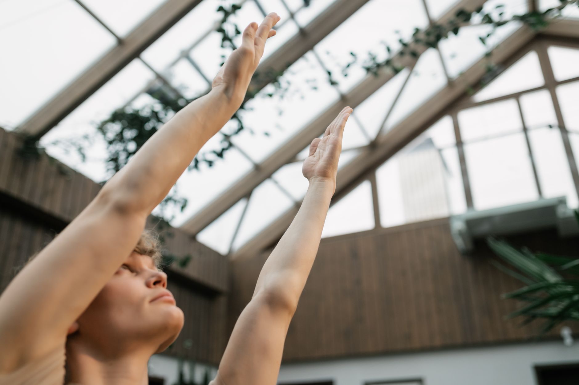 瑜珈如何幫助你度過情緒低潮:簡單技巧緩解壓力 Person practicing yoga indoors with arms raised in a glass-roofed room.