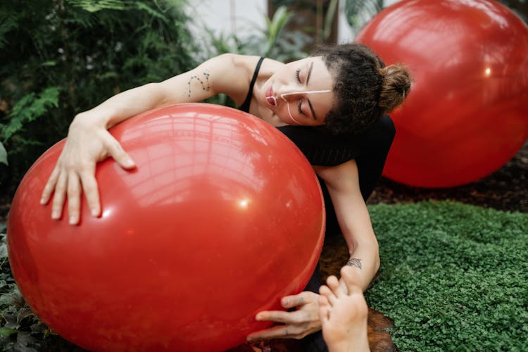 Woman Sitting Outdoors And Hugging A Giant Red Ball Wearing Creative Makeup 