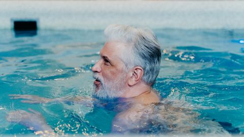 A senior man with grey hair swimming in a pool, enjoying leisure and relaxation.