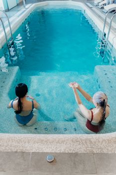 Two women enjoying a relaxing moment in an indoor swimming pool. Perfect for wellness and leisure themes.