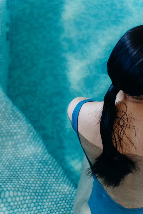 Free Aerial view of a woman in a blue swimsuit standing at the pool's edge, showcasing wet hair. Stock Photo