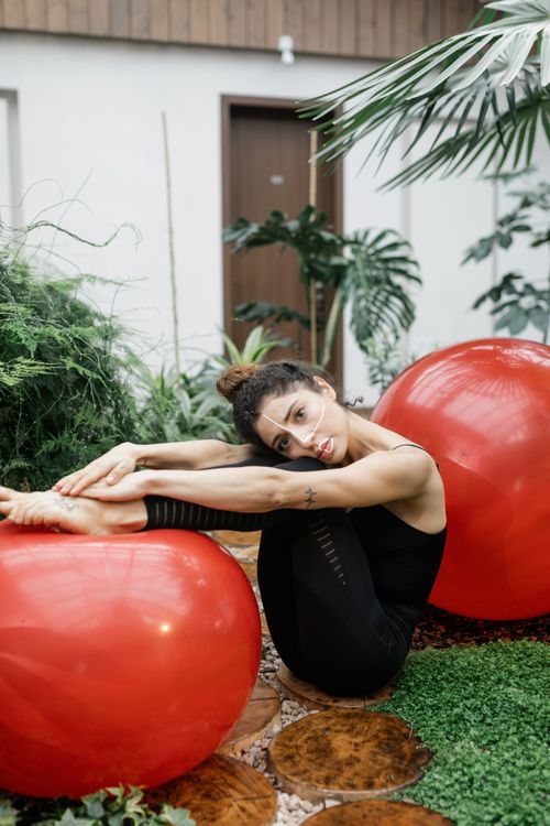 Free Woman practicing yoga with a red exercise ball in a lush indoor setting for a healthy lifestyle. Stock Photo