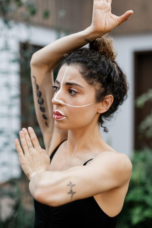 Free Woman practicing a unique dance pose outdoors with artistic face paint. Stock Photo