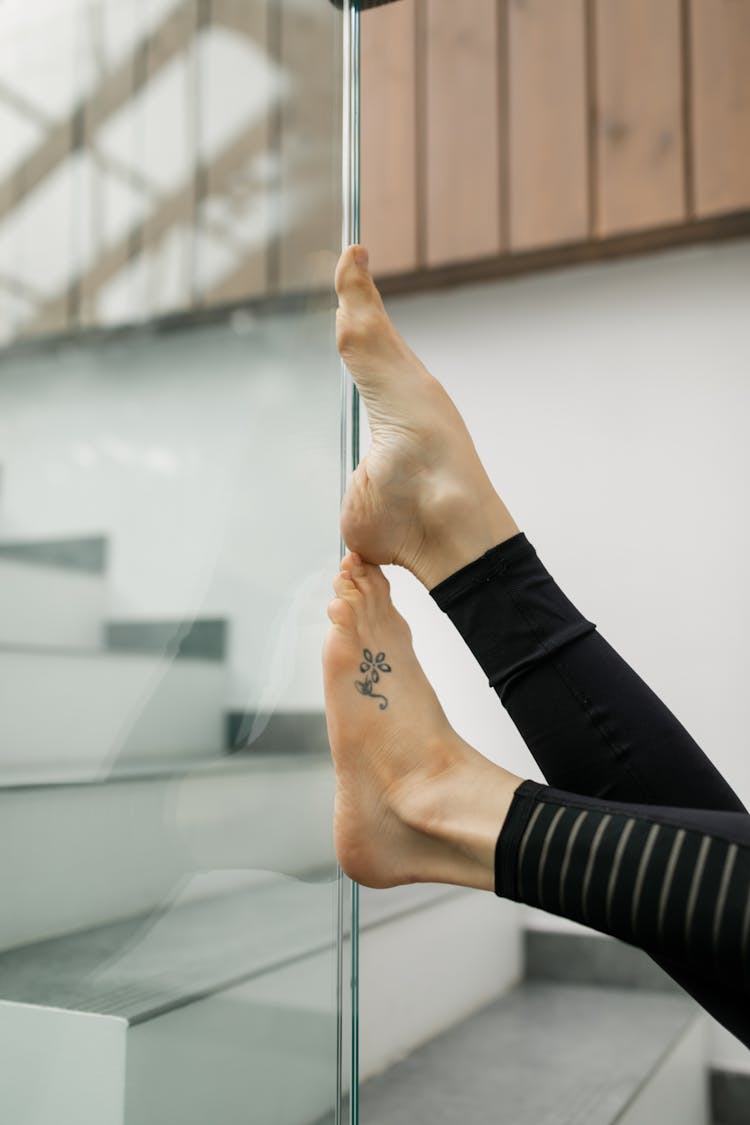 Woman Feet With Tattoo On Glass Wall