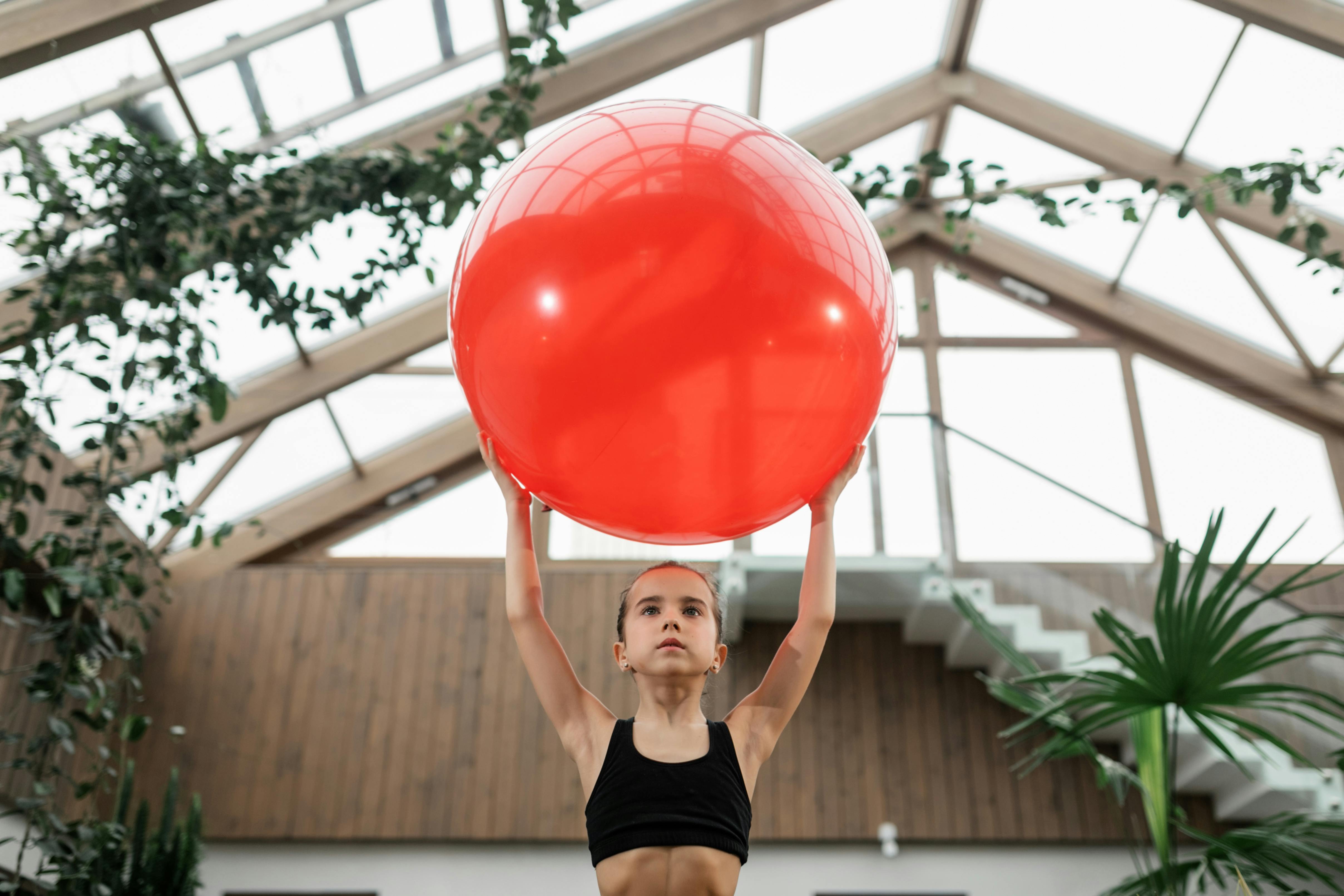 girl holding red fitness ball above head
