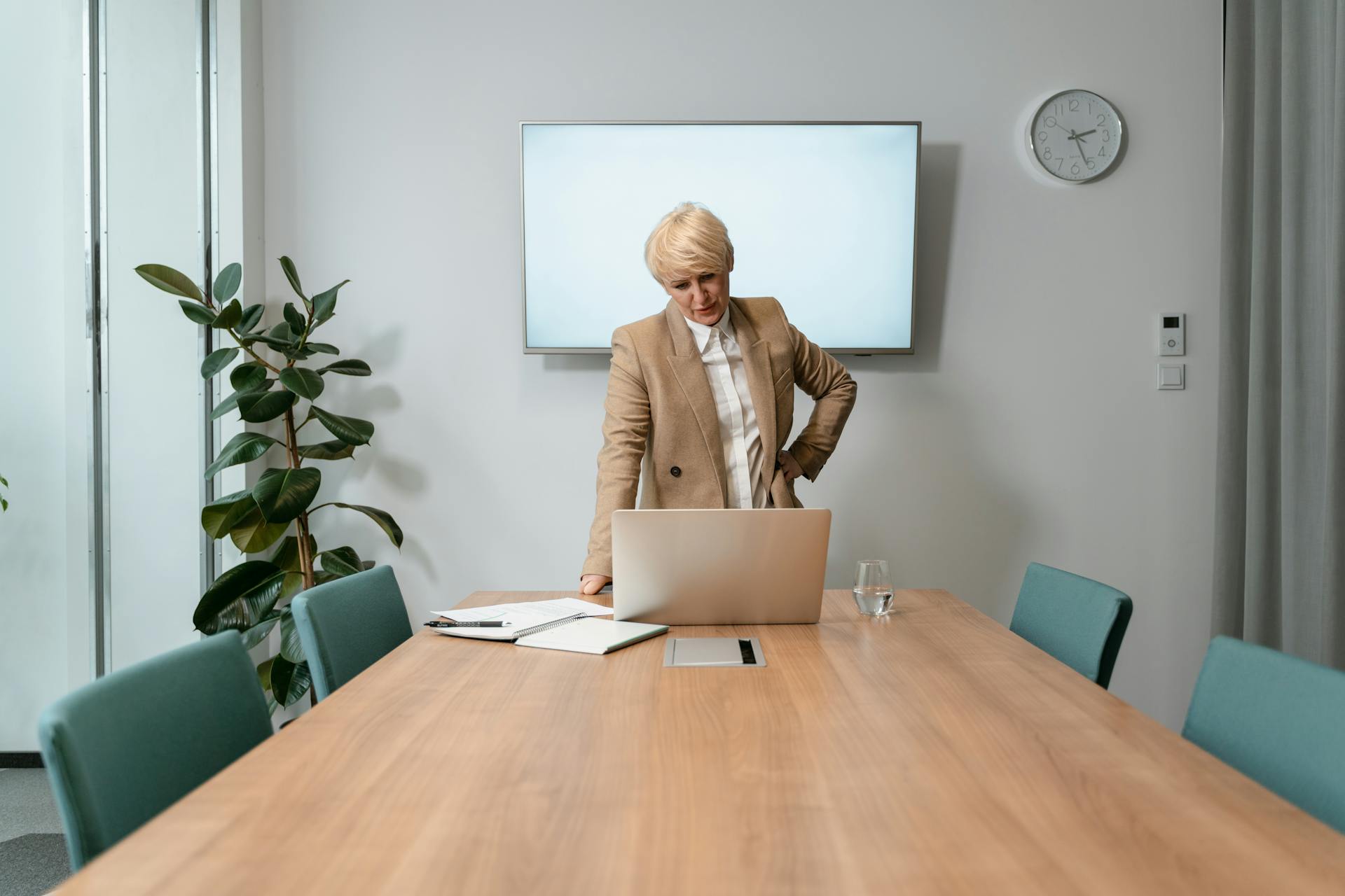 Professional businesswoman in corporate attire working on a laptop in a modern boardroom.