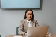 Woman in Gray Blazer Sitting on Chair in Front of Macbook
