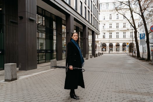 Caucasian woman in an elegant black coat posing with an umbrella on a city street.