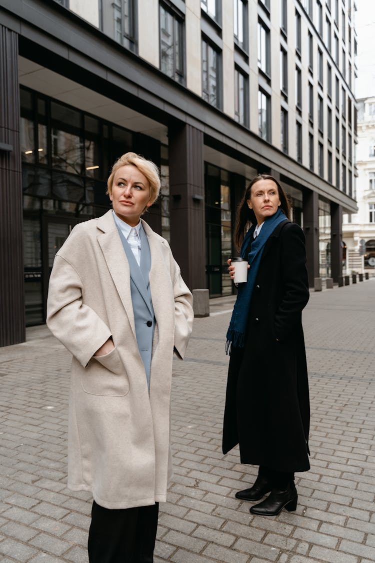 Two Women Wearing Coats Posing In The Street