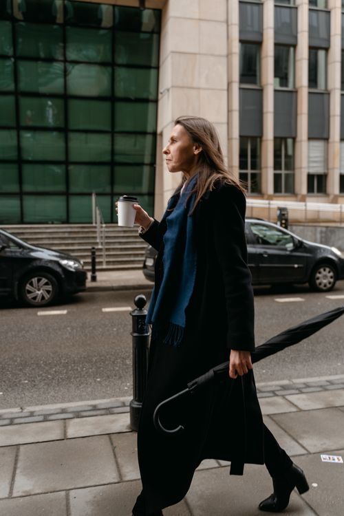 Free Side view of a woman walking with a coffee cup and umbrella on a city street. Stock Photo