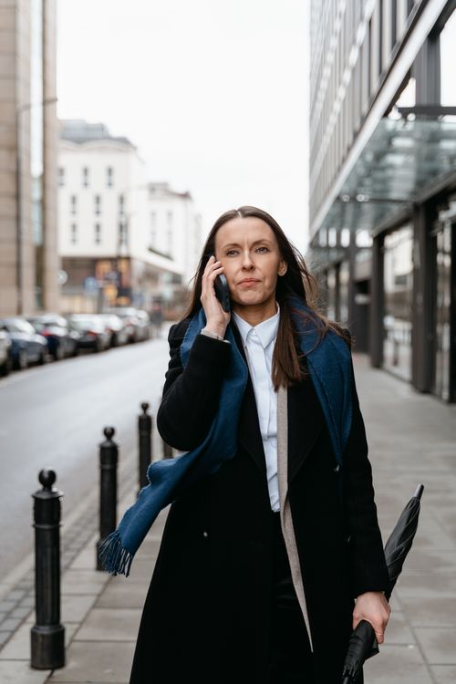 Free Professional woman walking in urban setting, engaged in cellphone conversation. Stock Photo
