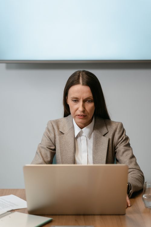 Free Professional woman in gray blazer concentrating on work at her laptop in modern office setting. Stock Photo