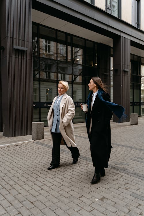 Women in Beige and Black Coat Walking on the Street while Having Conversation