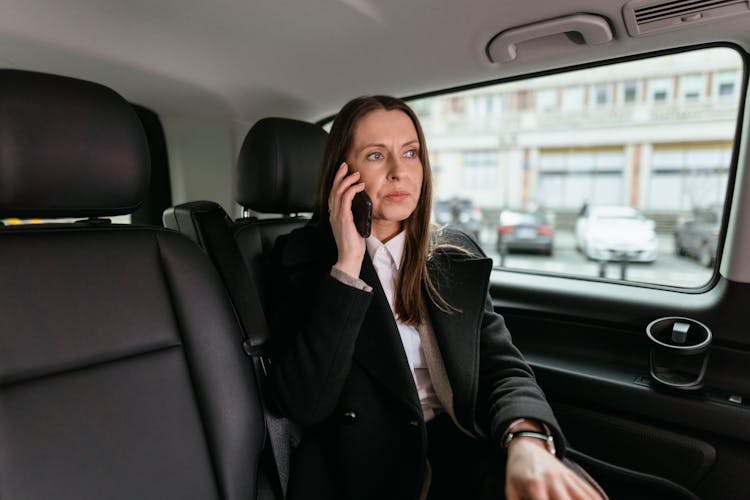 A Woman In Black Coat Sitting Inside The Car While Talking On The Phone