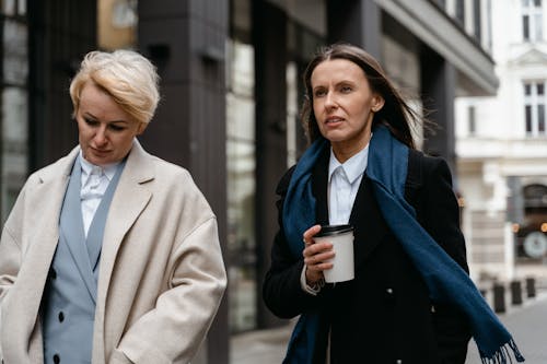 Free Women in Beige and Black Coat Walking on the Street while Having Conversation Stock Photo